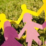 Paper people in various colours holding hands in the grass