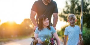 appears to be woman in wheelchair holding a young boy's hand (approximately 6 years old) and a man standing behind the woman and child