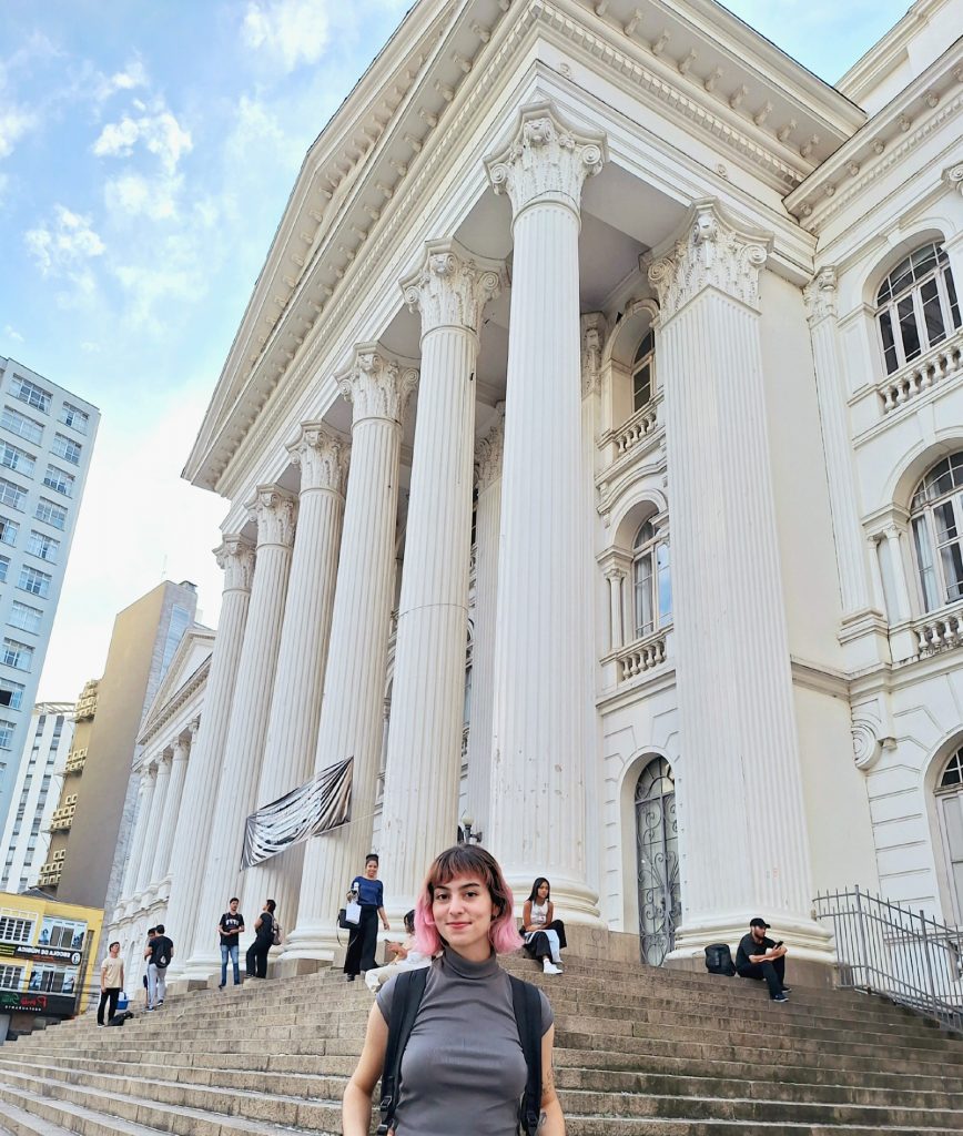 Jullye is standing in front of a large white 3-story building with colonial pillars