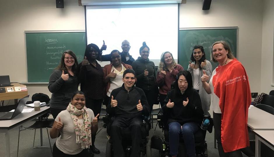group of students and service users posing for the camera with a thumbs up in front of a classroom screen