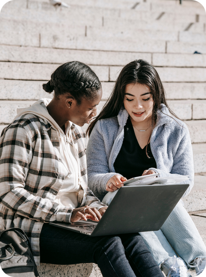 two people sitting on a bench looking at a laptop